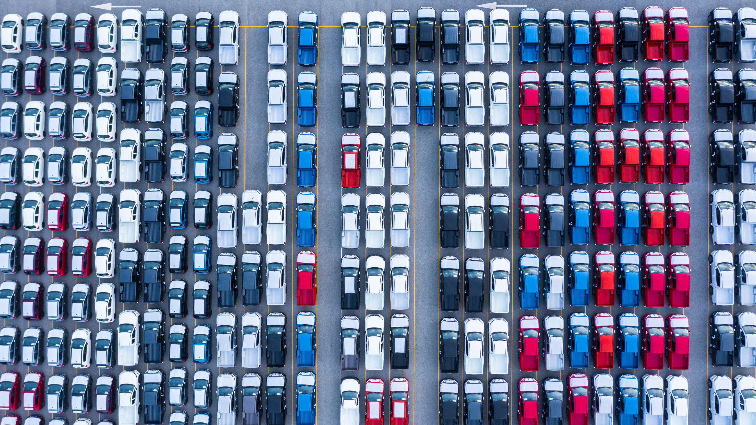 Vue aérienne de rangées serrées de voitures blanches, bleues et rouges sur un parc de stockage